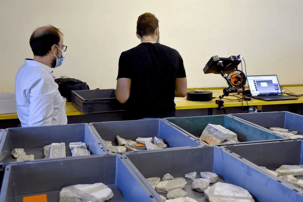 A robotic arm delicately places a fragment of a fresco under supervision in a lab at the Pompeii excavation site.